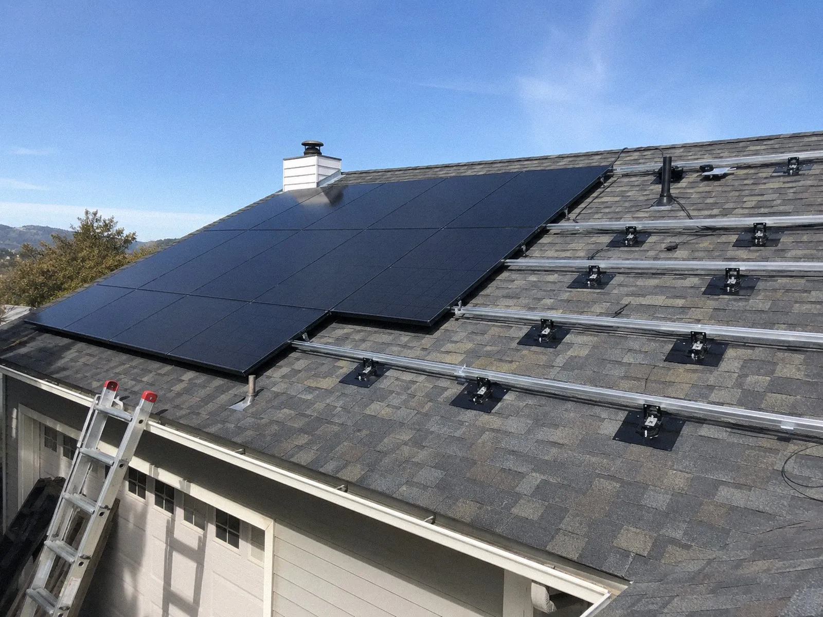 Installers mid-project on a composition shingle roof, panels and flashed mounting rails in place